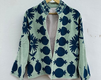 May include: A light green jacket with dark blue embroidered floral patterns. The jacket has a collar and open front, with a striped lining. The sleeves are three-quarter length, and the jacket is hanging on a wooden hanger.