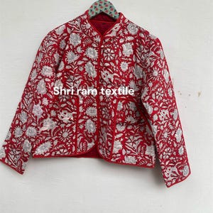 Könnte beinhalten: Rote Steppjacke mit weißem Blumenmuster. Die Jacke hat einen Stehkragen und ist rot gefüttert. Der Text "Shri ram textile" ist auf der Vorderseite aufgedruckt.