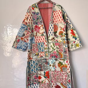 Puede incluir: Chaqueta tipo kimono patchwork con fondo crema y coloridos estampados florales. La chaqueta presenta un forro a rayas rojas y blancas, dos bolsillos delanteros y un corte holgado. Las mangas son de tres cuartos.