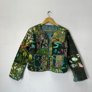 Pode incluir: Uma jaqueta acolchoada verde com um design de patchwork que apresenta vários motivos florais e animais. A jaqueta tem um decote em V, mangas compridas e fecho de zíper.