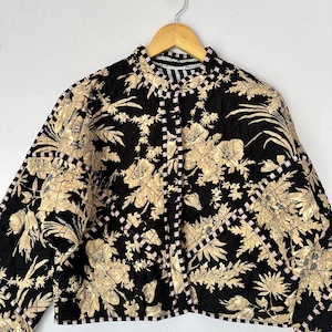 Peut inclure: Une veste matelassée noire avec un imprimé floral dans des tons beige et marron. La veste a un col montant et une fermeture boutonnée. Les coutures sont bordées d'un ruban rayé noir et blanc.