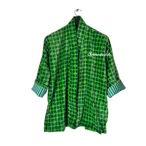 Op de afbeelding: Groene kimono-achtige badjas met een bladerenpatroon. De badjas heeft driekwart mouwen met gestreepte manchetten. De tekst "shriramtextile" is zichtbaar op de voorkant van de badjas. De badjas hangt aan een zwarte hanger tegen een witte achtergrond.