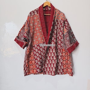 Op de afbeelding: Een patchwork kimono-jas in tinten bordeaux, oranje en crème. De jas heeft een mix van bloemen en geometrische patronen, met een effen bordeauxrode kraag en manchetten. De tekst "Shriramtextile" is zichtbaar op het kledingstuk.