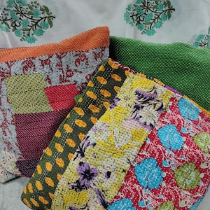 Può includere: Una collezione di cuscini decorativi patchwork colorati. I cuscini presentano vari motivi, tra cui disegni floreali e a pois, nelle tonalità di rosso, verde, giallo e arancione. Lo sfondo include un tessuto bianco con un motivo floreale turchese.