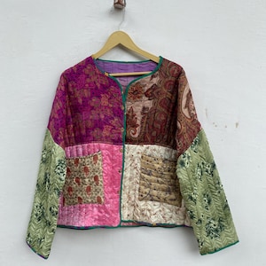 May include: A patchwork jacket with a round collar and long sleeves. The jacket features a mix of patterned fabrics in shades of pink, purple, brown, and green. It has a quilted texture and is trimmed with green piping.