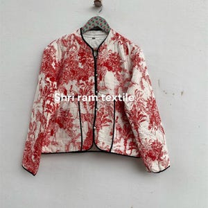Könnte beinhalten: Gesteppte Jacke mit einem rot-weißen Toile-de-Jouy-Muster mit Bäumen und Tieren. Die Jacke hat eine schwarze Paspel, einen runden Kragen und ist vorne geknöpft. Der Text "Shri ram textile" ist auf die Jacke gedruckt.