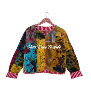 May include: A patchwork jacket with a variety of floral and patterned fabrics in shades of blue, yellow, and green. The jacket has long sleeves and a red and white striped trim. The text "Shri Ram Textile" is visible on the front.