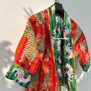 Może przedstawiać: Kolorowa pikowana kurtka z nadrukiem tygrysa i paskowanym wzorem. Kurtka ma długi, otwarty przód i jest wykonana z miękkiej, lekkiej tkaniny. Kurtka idealnie nadaje się do warstwowego ubierania i może być noszona na wiele sposobów.