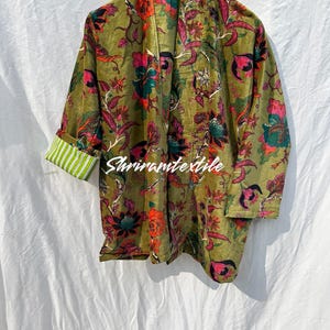 Op de afbeelding: Een groene fluwelen kimono met een bloemenprint in tinten roze, rood en zwart. De kimono heeft een brede kraag en lange mouwen.