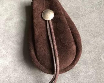 May include: A brown suede pouch with a silver button closure and a long brown leather cord.