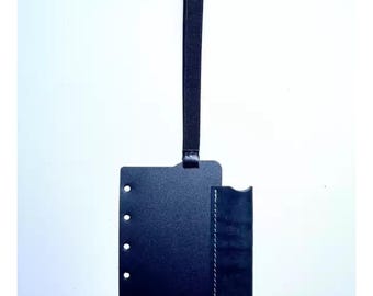 Könnte beinhalten: Ein schwarzes Ledergepäckanhänger mit einer Schlaufengriff. Der Anhänger hat eine rechteckige Form mit abgerundeten Ecken und eine Seitentasche. Auf der linken Seite befinden sich Löcher. Die Tasche ist mit weißem Faden genäht.