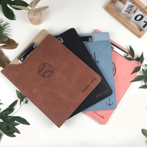 Könnte beinhalten: Vier personalisierte Leder-Klemmbretter mit verschiedenen Designs und Namen. Die Klemmbretter sind braun, schwarz, blau und rosa. Die Designs beinhalten einen Baseball, einen Anker und einen Buchstaben L. Die Namen sind Coach Larry, Prof. Lee, Samantha und ein unleserlicher Name.