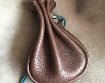 May include: A brown leather pouch with a drawstring closure and a textured, crocodile-like pattern. The pouch has a teal blue cord.