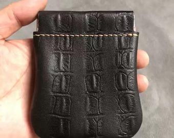 May include: A small black leather coin purse with a textured crocodile pattern. The purse has a stitched seam around the top edge.