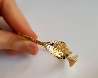 May include: A gold leaf-shaped bangle bracelet with small clear stones set along the edge.