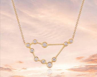 May include: A gold necklace with a constellation design featuring small, clear gemstones. The necklace is on a light pink and white background.