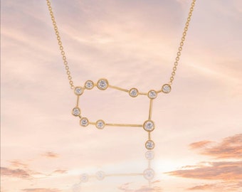 May include: A gold necklace with a constellation pendant featuring a design of the Gemini zodiac sign. The pendant is made of small, clear diamonds set in gold.