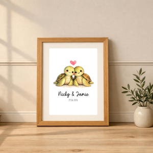 May include: A framed print featuring two green turtles side by side with a small pink heart above them. Below the turtles, the text reads "Nicky & Jamie" followed by the date "29.06.2026" in a simple black font on a white background.
