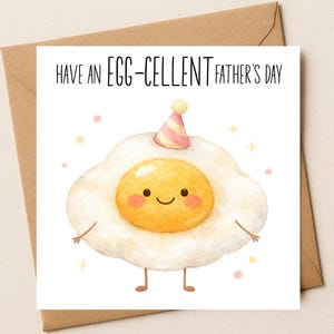 Puede incluir: Una tarjeta de felicitación cuadrada con una ilustración en acuarela de un huevo frito con cara sonriente, mejillas rosadas y un pequeño gorro de fiesta. El texto en la parte superior dice HAVE AN EGG-CELLENT FATHER'S DAY. La tarjeta está sobre un sobre marrón.