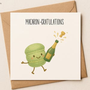 May include: A greeting card with a cartoon illustration of a green macaron holding a champagne bottle. The card reads "MACARON-GRATULATIONS" in black text. The card is on a beige background and is inside a brown envelope.