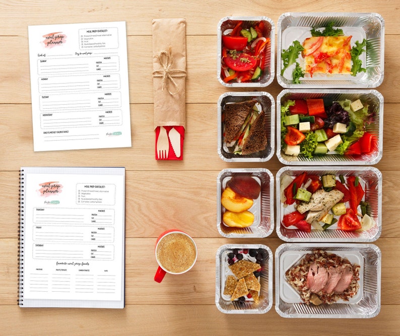 May include: A set of nine aluminum containers filled with various meal prep dishes. The containers are arranged on a wooden surface. The dishes include a salad with tomatoes and cucumbers, a salad with chicken and vegetables, a salad with fruit, a sandwich, a pasta dish with meat, and a rice dish with meat. There are also two meal prep planners on the surface.