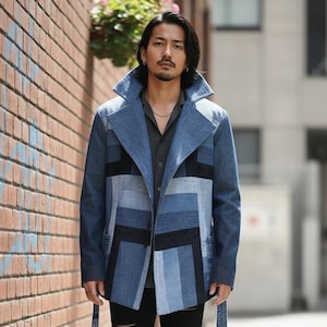 May include: A blue patchwork denim jacket with black accents, worn with black ripped jeans and black leather shoes. The jacket has a wide collar and a tailored fit. The outfit is completed with a dark grey button-down shirt.