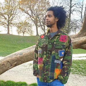 Könnte beinhalten: Tarnjacke mit bunten Patchwork-Details, darunter ein roter Stern und ein blauer Stern. Auf der Jacke steht der Text "ROYAL AIR FORCE". Die Person trägt eine blaue Jeans.