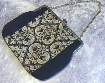 May include: A black and gold clutch purse with a chain strap. The purse has a floral pattern with gold accents.