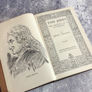 Puede incluir: Una ilustración en blanco y negro de Henry Fielding, el autor de Tom Jones, la historia de un niño encontrado. La ilustración es de un libro vintage con el título "Tom Jones" y el editor "Odhams Press Limited, Long Acre, London, W.C.2."