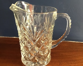 May include: A clear glass pitcher with a diamond pattern. The pitcher has a wide mouth and a handle.