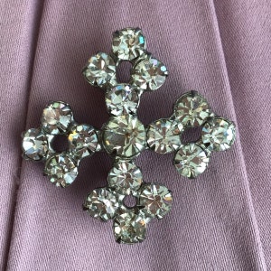 Può includere: Un fermaglio a forma di croce in argento con strass trasparenti. Gli strass sono disposti a forma di fiore.