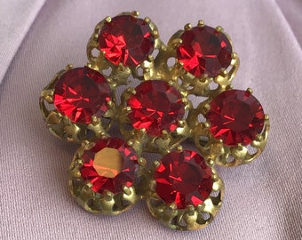 Könnte beinhalten: Eine goldfarbene Brosche mit einem Blumendesign mit sieben roten Glassteinen.