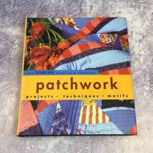 Può includere: Il libro della collezione Country Living Needlework intitolato "Patchwork: Progetti, Tecniche, Motivi" presenta una trapunta patchwork colorata sulla copertina. La trapunta è realizzata in tessuto rosso, blu e bianco.