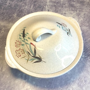May include: A white ceramic serving dish with a lid. The lid has a handle and a floral design with red, blue, and green accents. The dish is speckled with a light grey glaze.