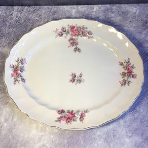 May include: A white oval serving platter with a gold rim and a floral design featuring pink roses and green leaves.