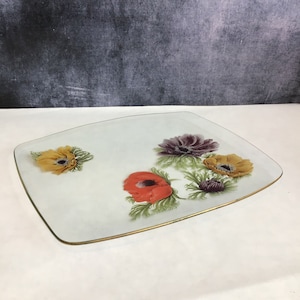 Puede incluir: Una bandeja de servir de vidrio transparente con un borde dorado presenta un diseño floral con flores rojas, amarillas y moradas.