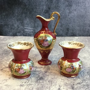 May include: Three red and gold porcelain vases with floral and romantic scene designs. The vases are decorated with gold trim and have a white interior.