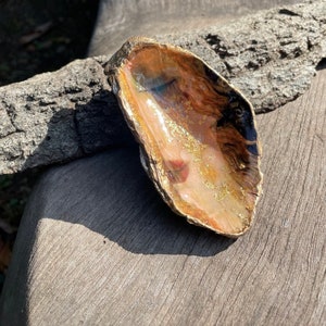 May include: A gold and pink seashell with a glossy finish and gold flecks. The shell is sitting on a piece of wood.