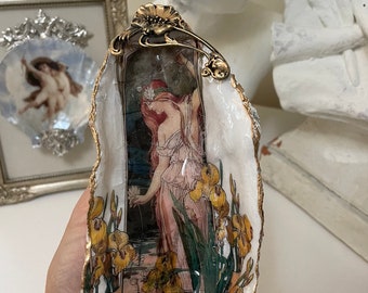 May include: A decorative oyster shell dish with a gold trim and a vintage image of a woman standing in a garden with yellow irises.