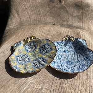 Könnte beinhalten: Zwei dekorative Keramikschalen in Form von Muscheln mit einem blauen und weißen geometrischen Muster und einem gelben und blauen geometrischen Muster. Die Schalen haben einen goldenen Rand und einen goldenen Akzent oben.
