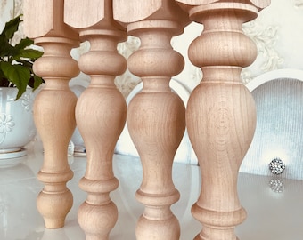 May include: Four unfinished wooden table legs with a turned design. The legs are square at the top and have a rounded, bulbous shape in the middle.