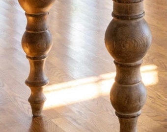 Puede incluir: Primer plano de una mesa de madera con patas torneadas. La mesa está hecha de madera marrón claro y tiene un acabado natural. Las patas están torneadas y tienen una forma bulbosa en la parte inferior.