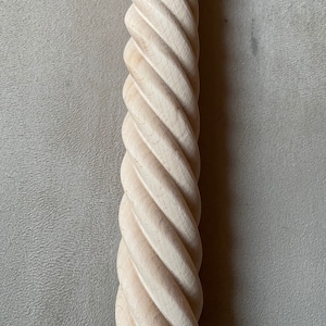 Puede incluir: Primer plano de una columna de madera retorcida, similar a una cuerda. La columna es de color marrón claro y tiene un acabado liso y pulido.