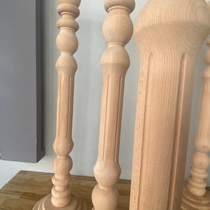 May include: Four wooden candle holders with a decorative, turned design. The candle holders are made of natural wood and have a light brown color.