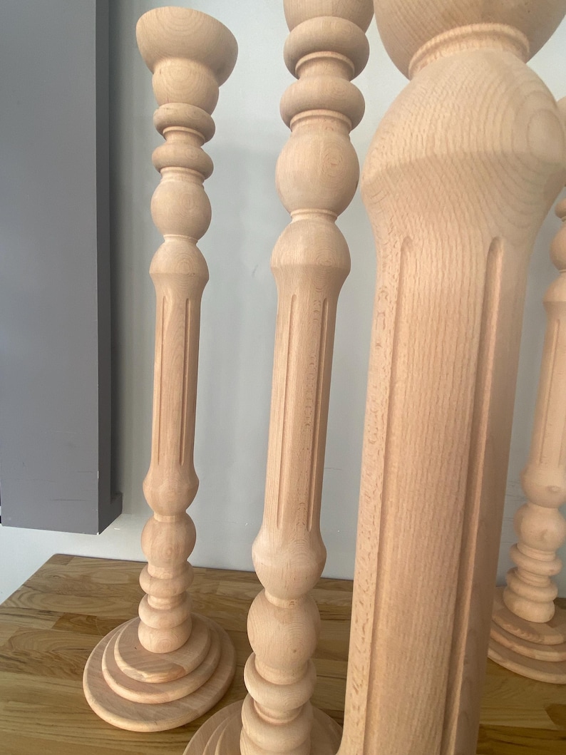 May include: Four wooden candle holders with a decorative, turned design. The candle holders are made of natural wood and have a light brown color.