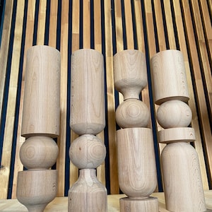 May include: Four wooden candle holders with different designs. Each holder is made of natural wood and has a unique shape. The holders are arranged in a row on a wooden surface.