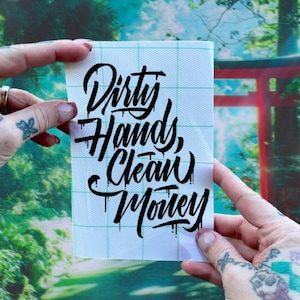 May include: A white sticker with black lettering that reads "Dirty Hands, Clean Money".