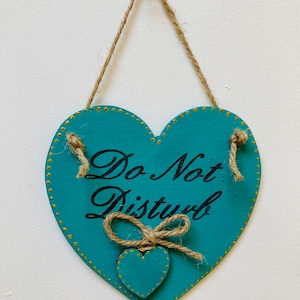 May include: A teal blue wooden heart-shaped sign with gold glitter trim and a smaller teal blue heart in the center. The sign says "Do Not Disturb" in black lettering.