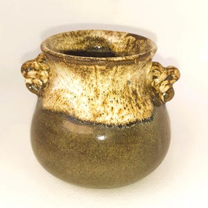 May include: A small ceramic vase with a rounded body and two small handles. The vase has a two-tone glaze, with a dark brown base and a lighter, speckled tan upper section. The interior is dark brown.