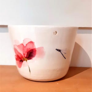 May include: White ceramic mug featuring a pink flower and a dragonfly design.